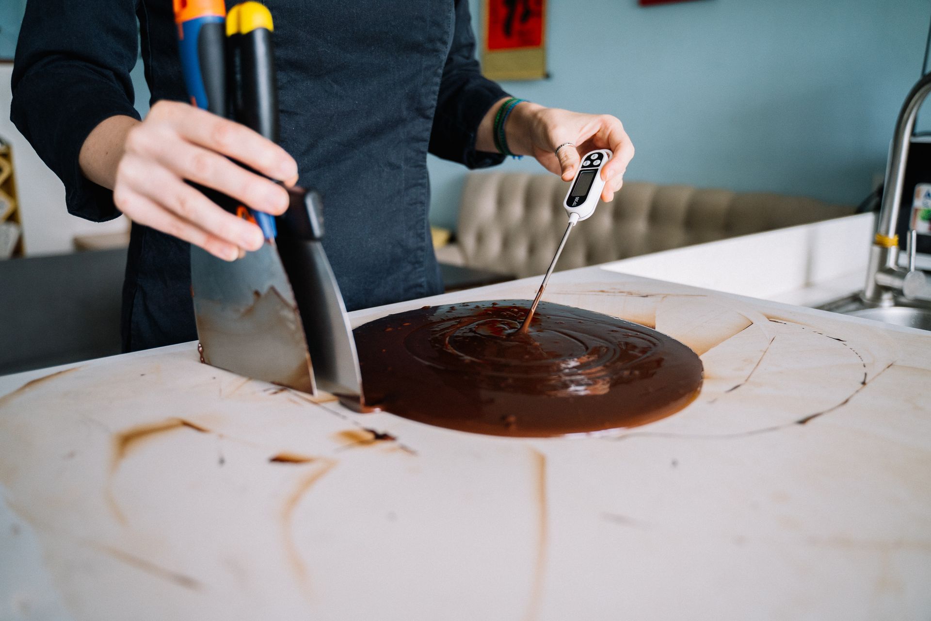 A chocolatier spreading tempered chocolate on a marble slab and checking its temperature