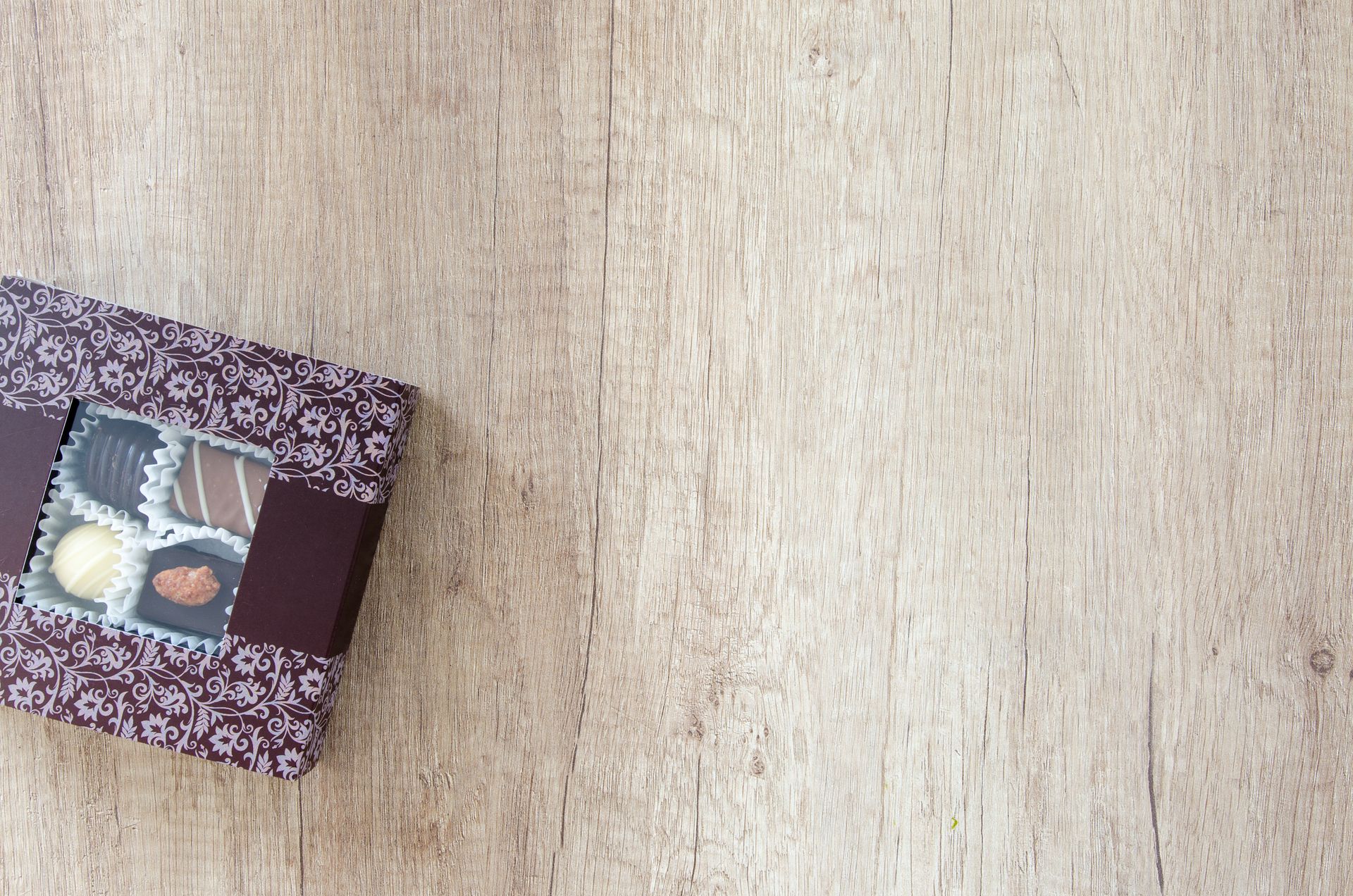 A small box of filled chocolates on a pale wooden table